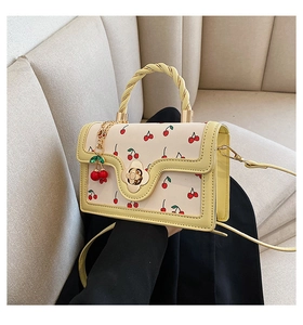 Detail of cream leather handbag featuring red cherry patterns and yellow twist handle