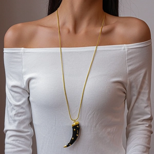Macro detail of a black horn pendant with gold dots on a long necklace worn by a model