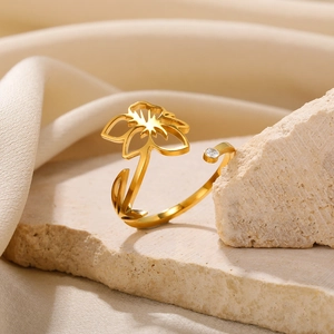 Close-up of golden stainless steel open flower ring with zircon detail on stone background