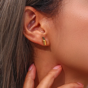 Close-up of golden beverage cup earrings with green crystals worn by a model