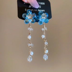 Detail of blue crystal flower earrings with dangling pearl and gold tassels