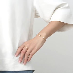 Bracelet double couche en acier titane doré avec perles blanches sur un poignet féminin