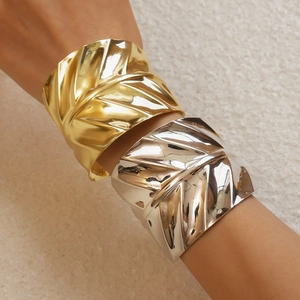 Detailed macro view of geometric leaf texture on gold and silver wide cuff bracelets