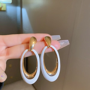 Macro shot of large oval drop earrings in gold metal and white enamel for women