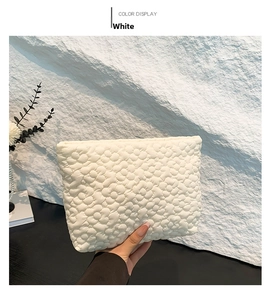 Detailed close-up of white quilted handbag with 3D floral texture on black table