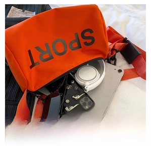 Vue détaillée du sac bandoulière orange contenant un téléphone, un casque et des lunettes