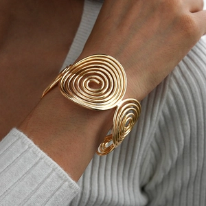 Detail of chunky gold geometric spiral cuff bracelet styled with white knitwear