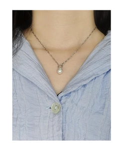 Close-up of a white pearl pendant necklace on a silver chain worn by a woman