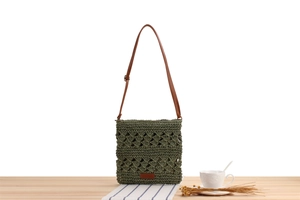 Close-up of green woven beach bag with brown leather strap on a rustic wooden table