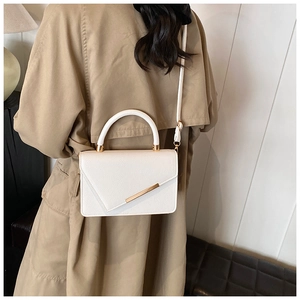 Detail of a white leather envelope handbag with gold hardware and top handle on a trench coat
