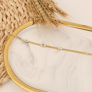Golden snake chain bracelet with evil eye charms on white marble tray with wheat decor
