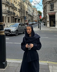 Dettaglio di un cappotto lungo in lana a righe nere con cappuccio e design a sciarpa