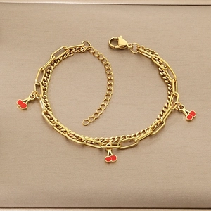 Detail of gold layered chain bracelet featuring red cherry charms and lobster clasp closure