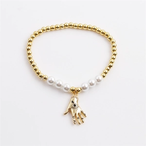 Gold beaded hamsa hand bracelet with pearls and evil eye charm on white background