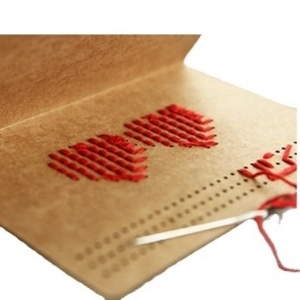 Handmade DIY kraft paper greeting card with red cross-stitch heart design and needle