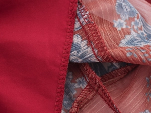 Gros plan détaillé montrant les coutures de précision sur tissu rouge et mousseline