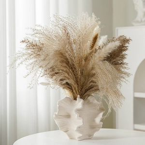 European white ceramic vase with matte texture and decorative dried reeds on a table