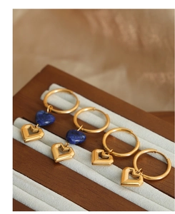 Detail of gold hollow heart earrings with blue gemstone drops on beige velvet tray