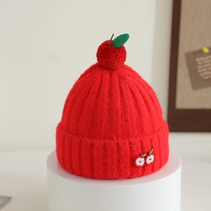 Detail of red apple knit hat featuring leaf decor and cherry embroidery on white stand