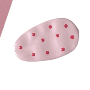 Pink polka dot hair clip with wavy edges and glossy finish on a minimalist background