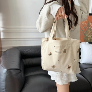 Detail of cream corduroy tote bag featuring brown teddy bear embroidery and double handles