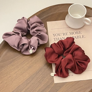 Detail of grey-purple and deep red satin scrunchies with elegant gold logo tags