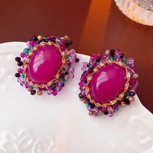 Close-up of vintage oval purple gemstone earrings with gold metal on white embossed plate