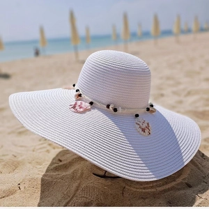 Detail of white wide brim straw hat with seashells and black beads on a beach