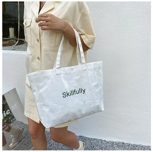 Outdoor shot of a large white jelly tote bag featuring green Skillfully typography detail