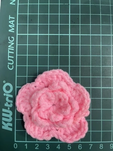 Detailed top view of a 7cm pink three-layer crochet flower on a green scale mat
