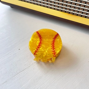 Macro detail of a yellow baseball-shaped hair claw with glossy pearl texture and red stitching