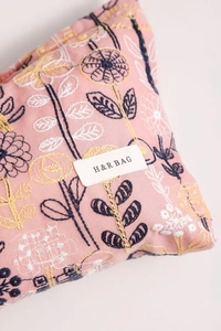 Macro detail of floral embroidery and branded woven label on pink fabric cosmetic bag