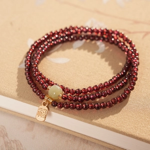 Detail of red garnet multi-layer bracelet with green jade bead and gold Fu charm
