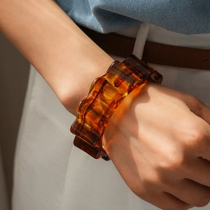 Dettaglio di un bracciale in acrilico ambra con texture geometrica ondulata sul polso