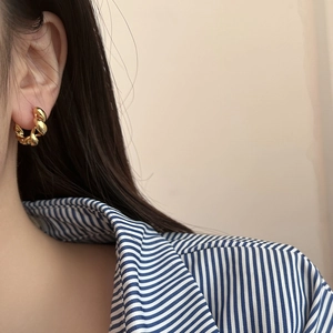 Elegant gold twisted croissant hoop earrings worn by a model in a minimalist style