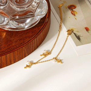 Detail of golden cross charms and white pearls on a minimalist stainless steel bracelet