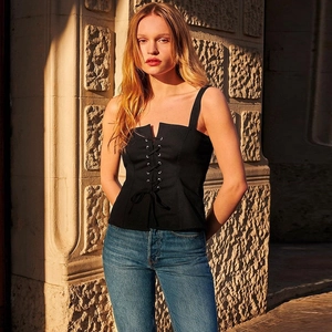 Top corto negro sexy con cordones y jeans frente a una pared de piedra con luz solar