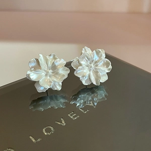 Elegant creamy white floral stud earrings with pearl luster on a reflective surface