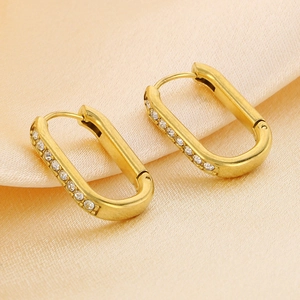 Gold oval hoop earrings with sparkling white cubic zirconia on light silk background