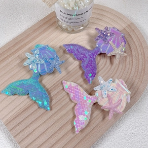 Close-up of sequin mermaid tail hair clips with seashell details on a wood tray