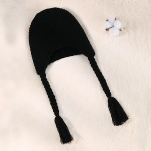 Detail shot of black knitted baby hat featuring braided tassels on soft white faux fur