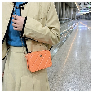 Detail view of a glossy orange quilted PVC crossbody bag with golden chain strap