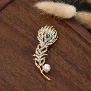 Macro detail of peacock feather brooch with sparkling zircons and a green teardrop gem