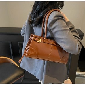 Brown leather shoulder bag with buckle strap detail worn by model in minimalist setting