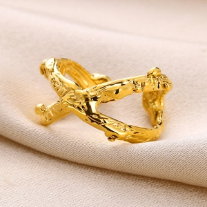 Close-up of gold X-shaped cross ring with irregular textured surface on silk fabric
