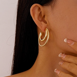 Detail of model wearing gold double-layered C-shaped earrings with woven texture