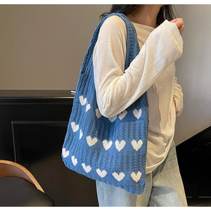 Primer plano de un bolso de punto azul con corazones blancos llevado al hombro
