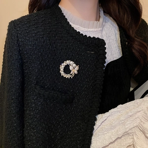 Détail de la broche fleur perle et papillon sur une veste en tweed noir élégante