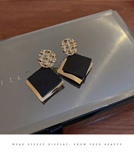 Close-up of geometric gold and black earrings with woven ring and square dangles
