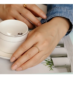 Detail showing a golden twisted rope ring worn by a model holding a white coffee cup